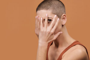 Woman with shaved head hiding behind fingers