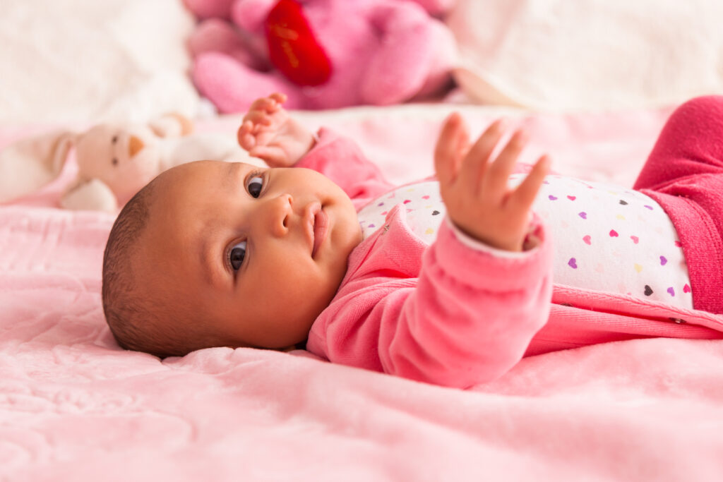 Adorable black baby girl in pink pajamas on pink bed