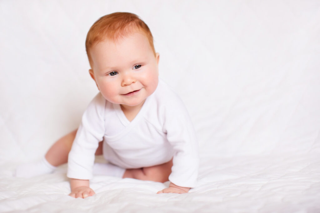 Little cute baby girl in white romper in bedroom